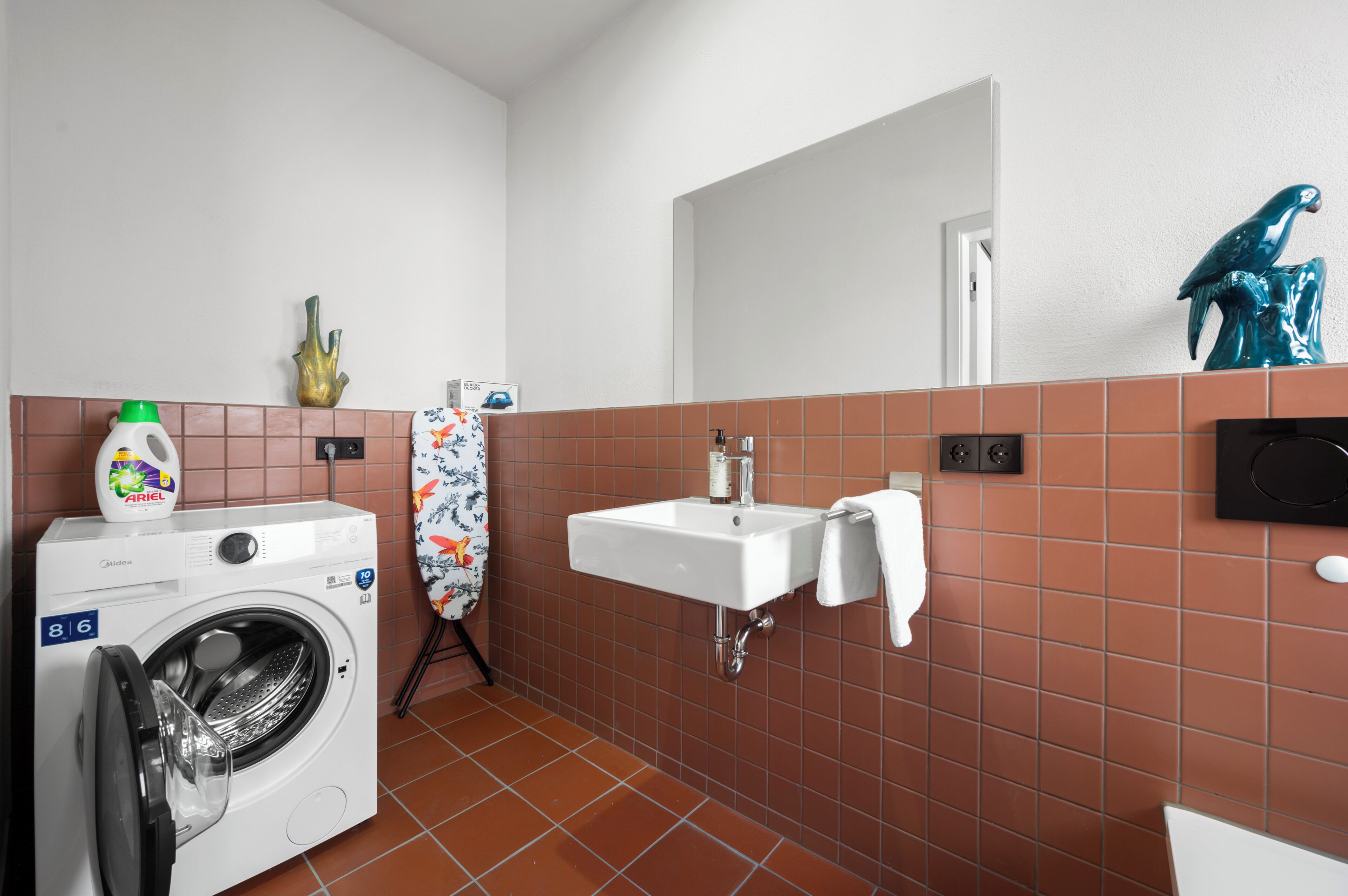 A compact bathroom with a washing machine, a sink, and a towel rack.