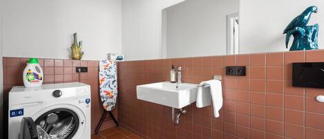 A compact bathroom with a washing machine, a sink, and a towel rack.
