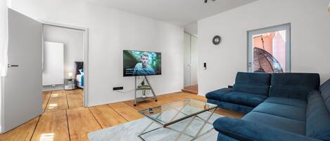 A modern living room with a blue sofa, a glass coffee table, and a flat-screen TV.