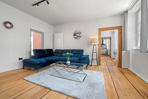 A modern living room with a blue sectional sofa, a glass coffee table, a white rug, and a wooden floor. - LiT LiVING Grünstadt (Grünstadt)