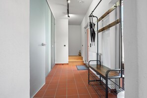 Ein Flur mit Fliesenboden, einer Holztreppe, einer Metallbank und einem an der Wand befestigten Regal mit Schirmen.