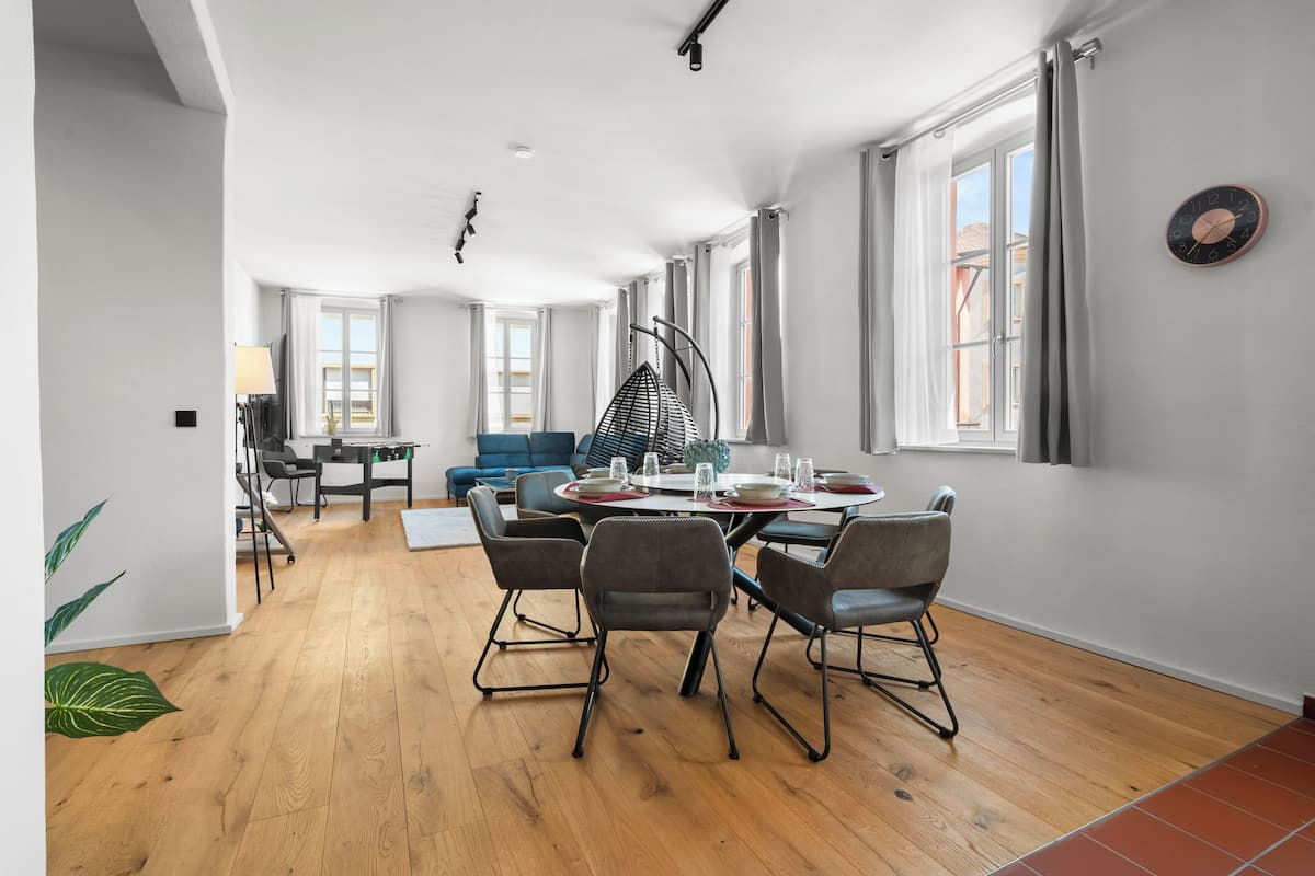 A spacious living area with a dining table set for four, a blue sofa, and a hanging chair.
