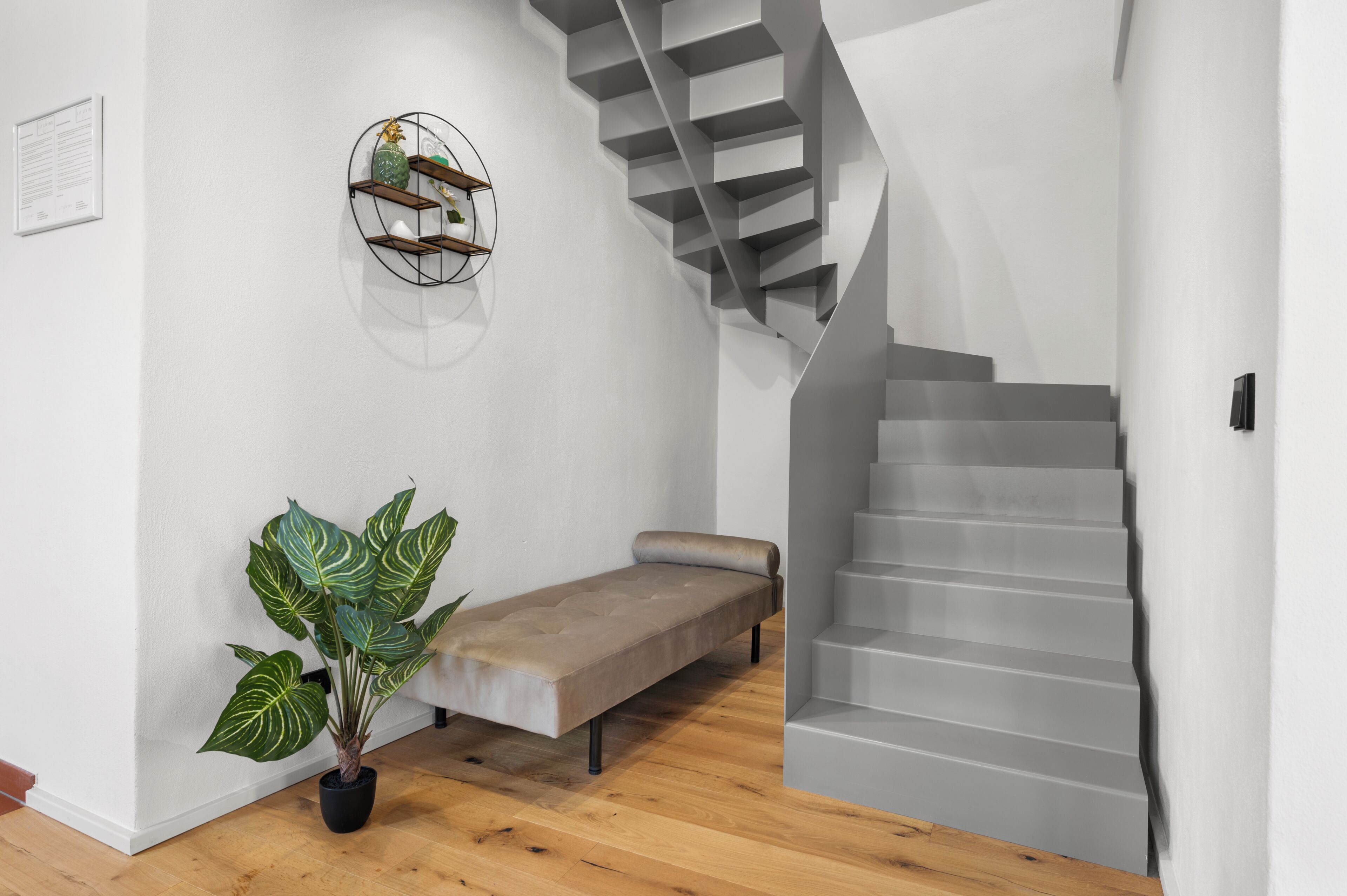 A modern interior with a staircase, a bench, a potted plant, and a wall-mounted shelf.