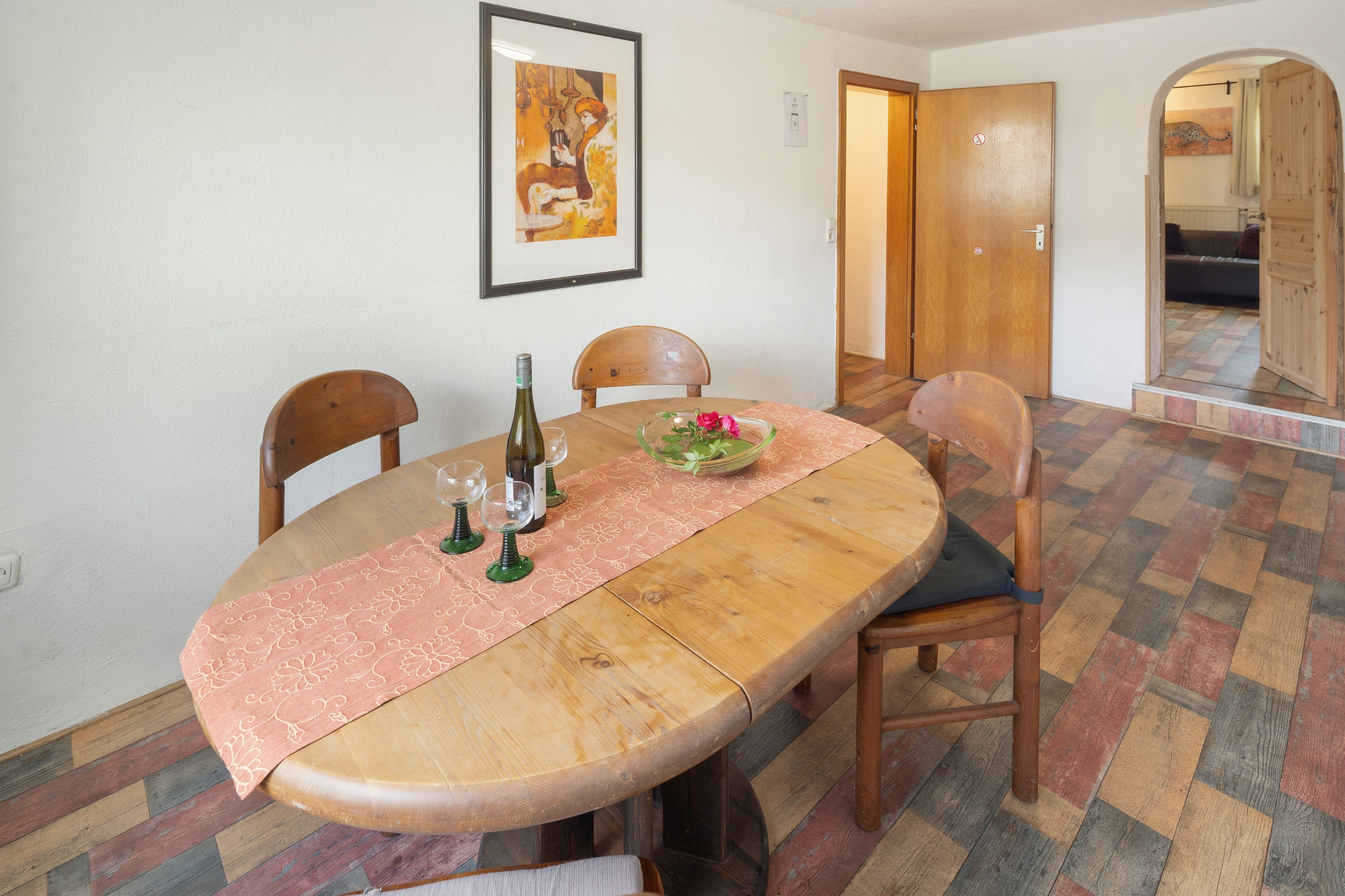Un comedor con una mesa de madera, sillas, un jarrón de cristal con flores y un cuadro en la pared.
