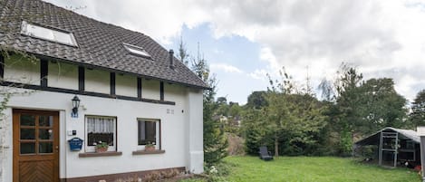 A white house with a tiled roof, a wooden door, and a small garden.