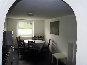 Un coin repas comprenant une table ronde, quatre chaises, une fenêtre, un tableau accroché au mur et une petite table blanche.
