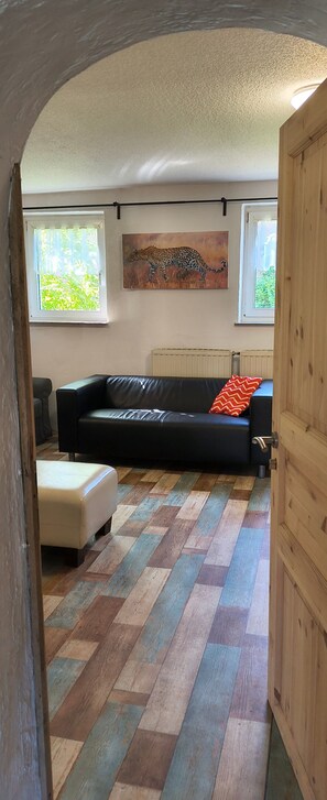Ein Zimmer mit einer schwarzen Ledersofa, einem weißen Ottomanen, einem Holzschrank, einem Heizkörper und einem Leopardenbild.
