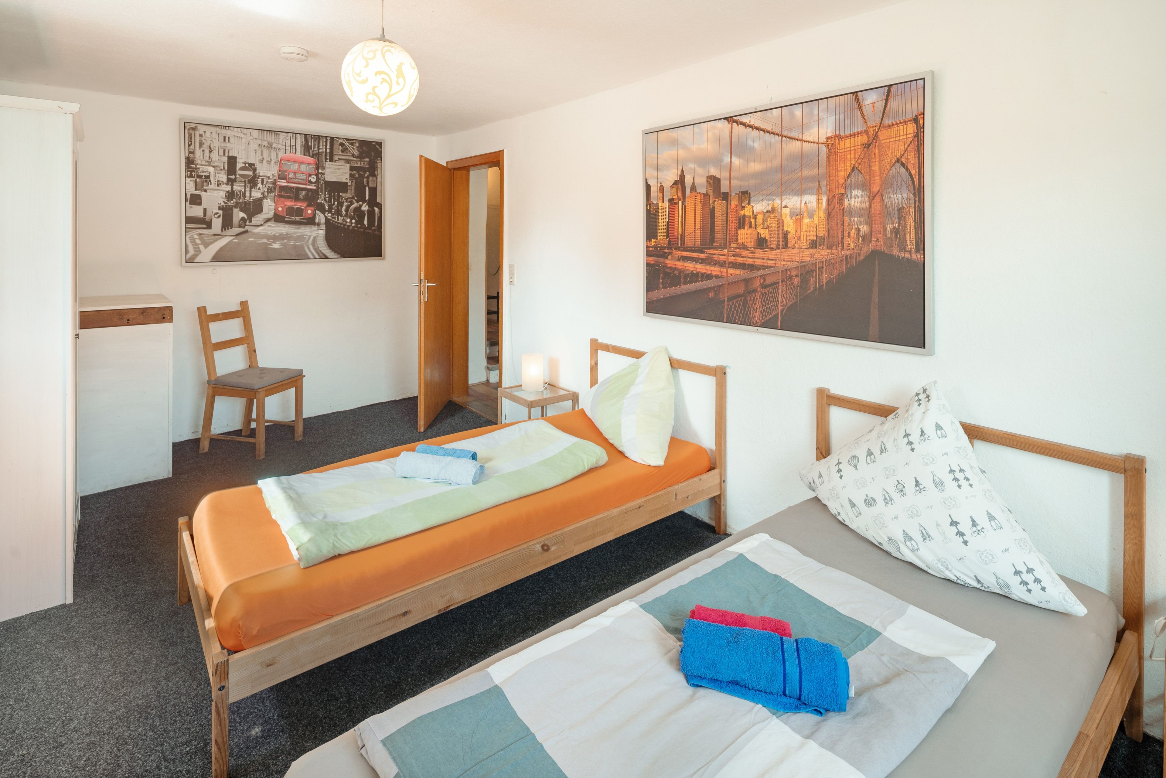 Ein Schlafzimmer mit einem Bett, einem Sessel, einem Nachttisch mit Lampe und zwei Wandbildern.