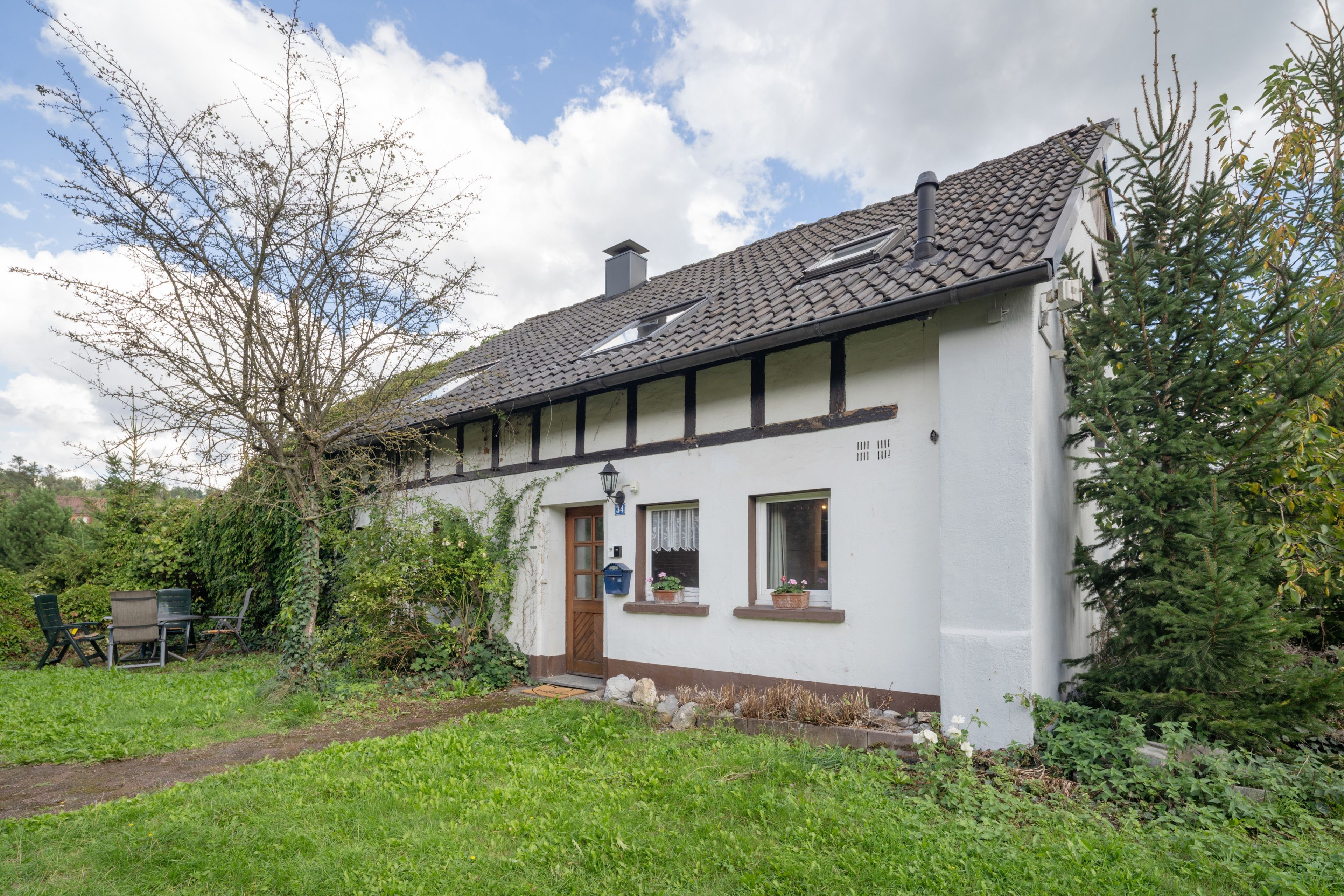 Ein weißes Gebäude mit einem Ziegeldach, einer Holztür und zwei Fenstern mit Blumenkästen.