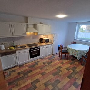 Et kompakt køkken med hvide skabe, en mikrobølgeovn, kaffemaskine og et spiseområde med bord og stole.