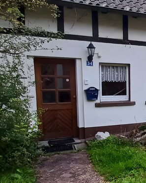 En hvid bygning med en brun dør, et vindue med blondegardin og et skilt med nummer 34.