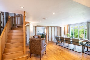 A spacious living area with a wooden staircase, a dining table with chairs, and a kitchen in the background. - Wolmers Barn, Stonham Aspal, Suffolk (Stonham Aspal)