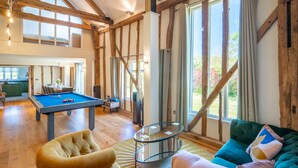 Una habitación amplia con mesa de billar, un sofá cómodo y grandes ventanales con vistas al exterior.