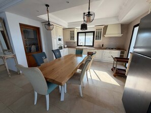 A modern kitchen with white cabinets, a wooden dining table, and a stainless steel refrigerator.