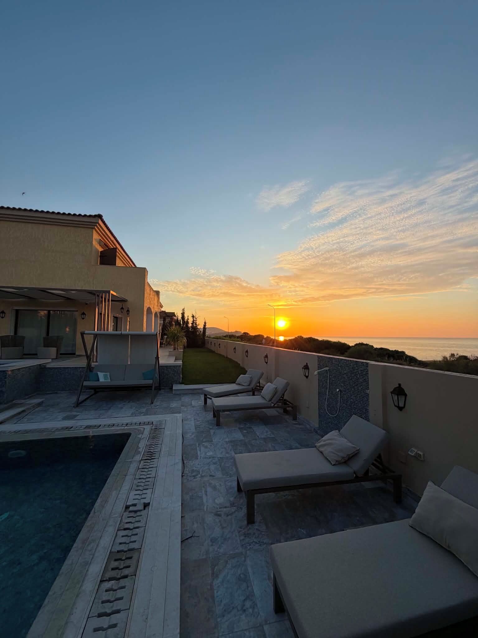 Zona de piscina en la azotea con sillas de descanso y vistas a la puesta de sol sobre el océano.