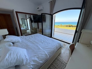 A bedroom with a bed, a TV, and a view of the sea.