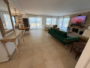 A spacious living room with a green sofa, a wooden coffee table, a TV mounted on the wall, and a fireplace.