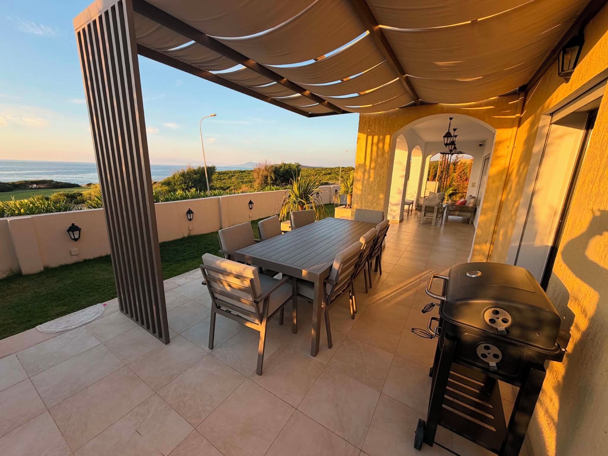 Un patio al aire libre con mesa y sillas, una parrilla y vista al océano.