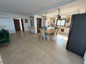 A spacious living area with a dining table and chairs, a kitchen with white cabinets, and a large window.