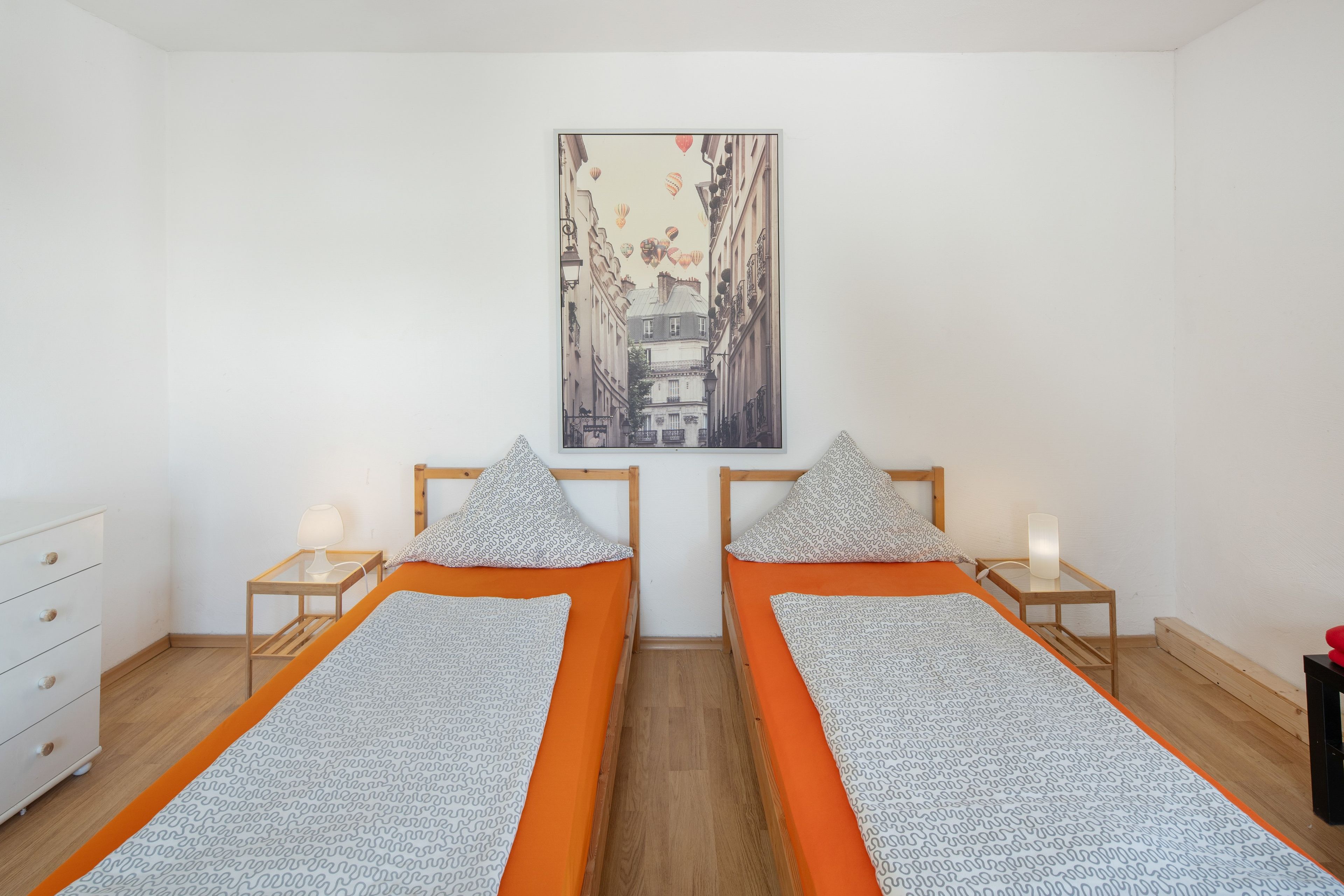 Ein Zimmer mit zwei Einzelbetten, einem weißen Schminktisch, einem Stadtbildgemälde und Holzboden.