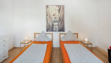 Ein Zimmer mit zwei Einzelbetten, einem weißen Schminktisch, einem Stadtbildgemälde und Holzboden.