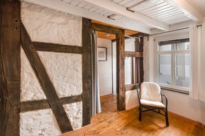 A room with exposed wooden beams, a chair, and a window with blinds. - Mammut Loft Apartment (Balve)