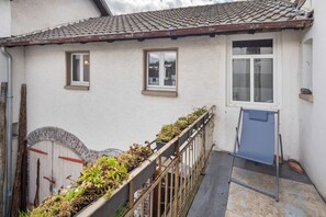 Ein weißes Gebäude mit Ziegeldach, zwei Fenstern, einer Tür und einem kleinen Balkon mit Pflanzen.