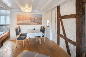 Ein gemütliches Zimmer mit Holzboden, einem Tisch mit Stühlen, einem Strandbild und einem Fenster mit Blick.