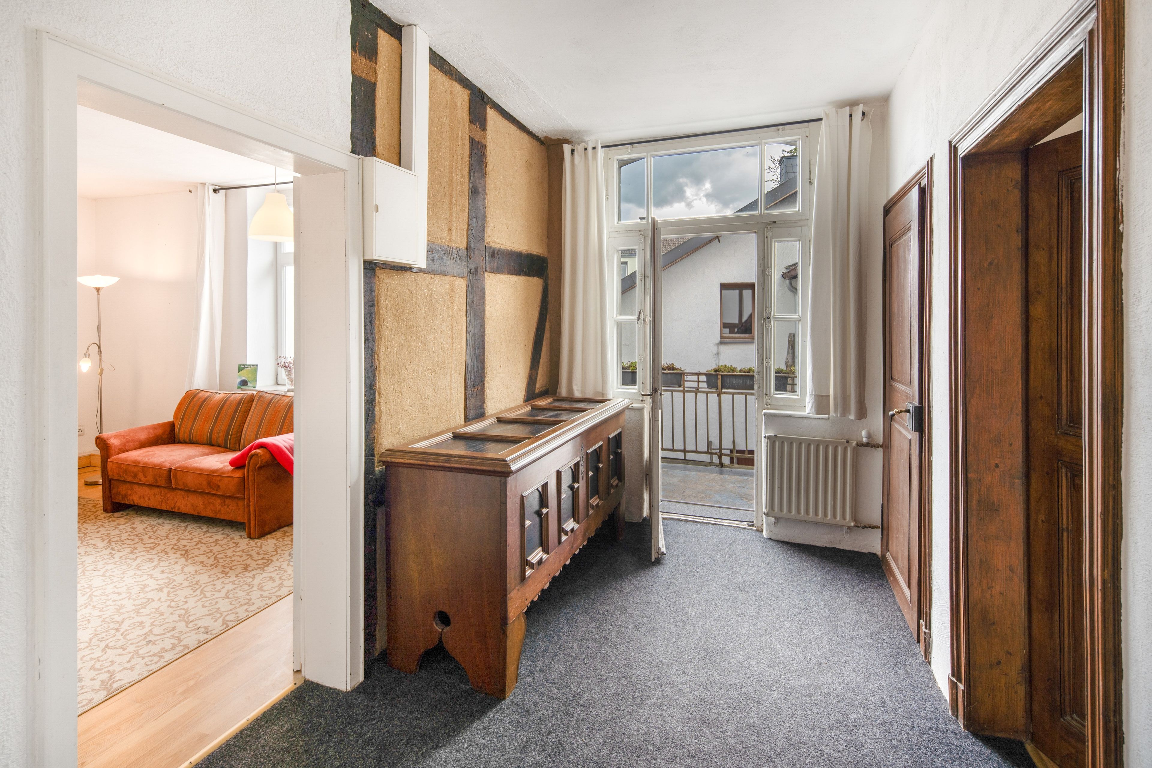 Ein Flur mit einem Holzschrank, einem roten Sofa und Blick in einen Raum mit einem Fenster.