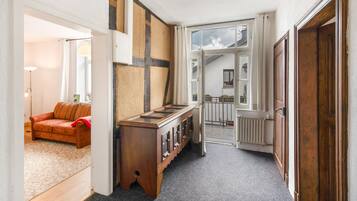 Ein Flur mit einem Holzschrank, einem roten Sofa und Blick in einen Raum mit einem Fenster.