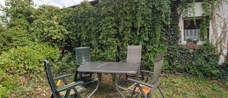 Un espace extérieur aménagé avec une table et des chaises, entouré d’une végétation luxuriante et bordé d’un bâtiment dont les murs sont recouverts de lierre.