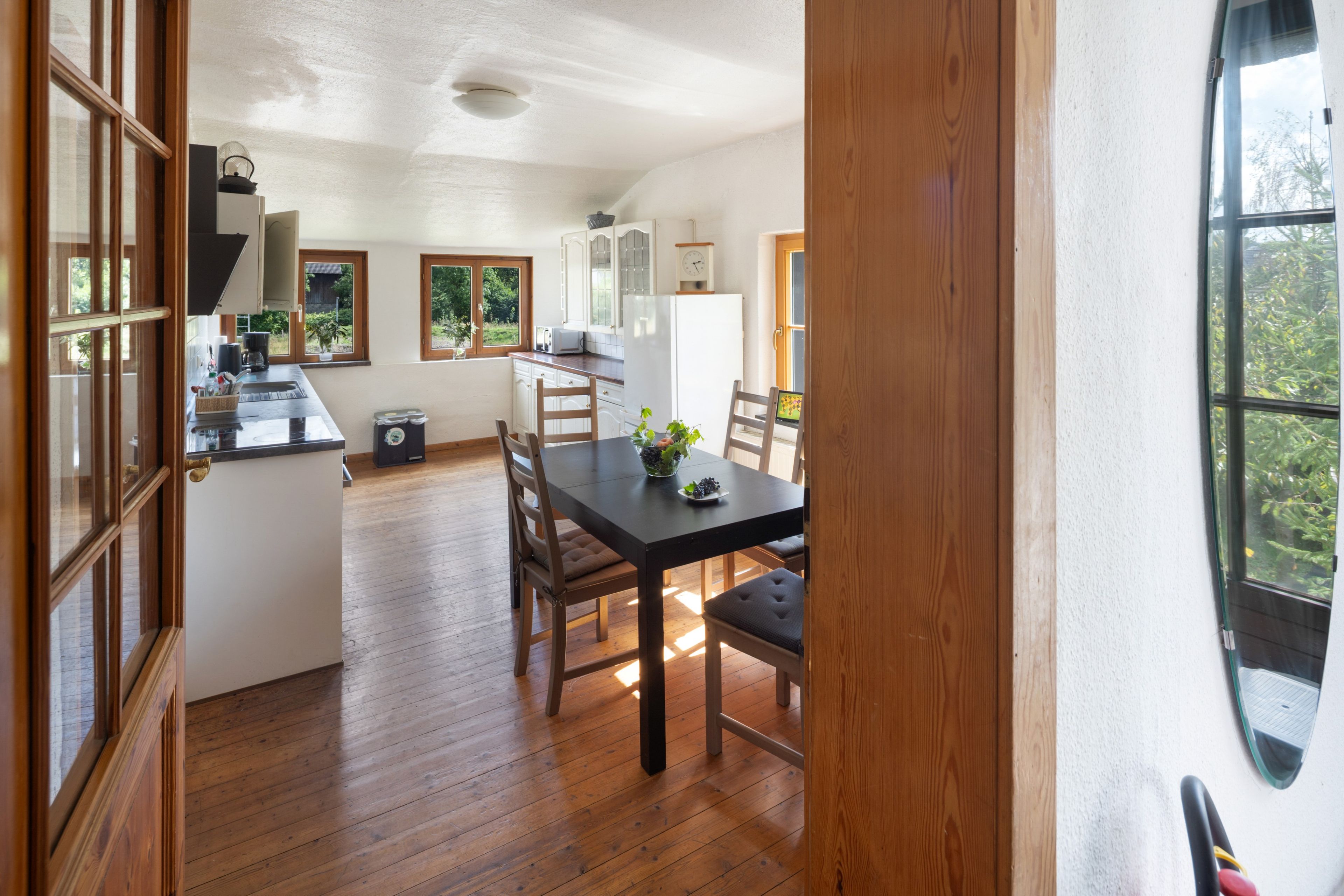 Une cuisine avec des meubles en bois, une table à manger avec des chaises et une vue sur l’extérieur par les fenêtres.