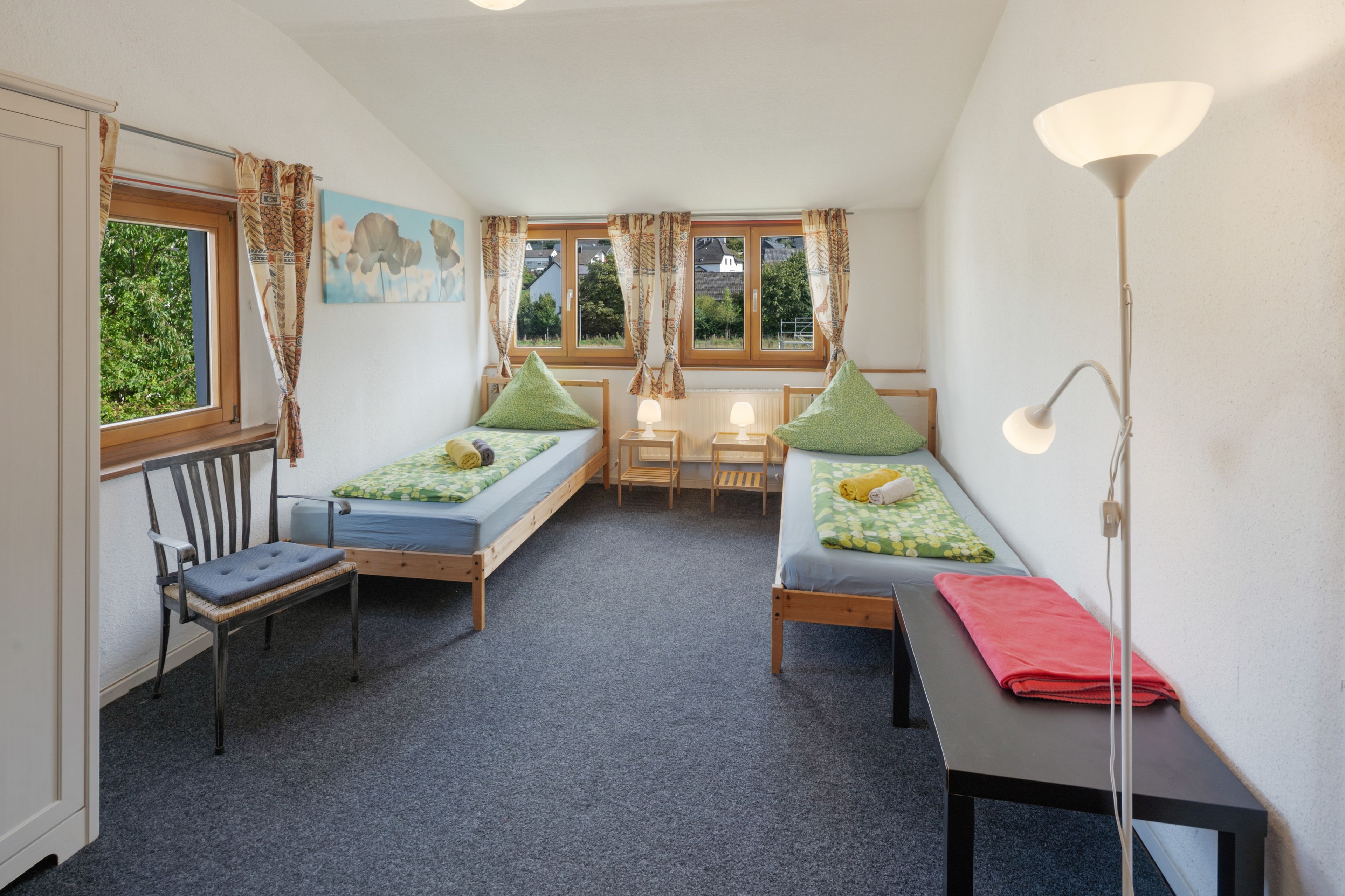 Ein Schlafraum mit zwei Einzelbetten, einem Stuhl, einem Tisch und einer Lampe.