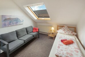 Ein kleiner, gut beleuchteter Raum mit einem grauen Sofa, einem Bett mit floralem Bettbezug, einem Oberlicht, einem Heizkörper und einem Leopardenbild an der Wand.
