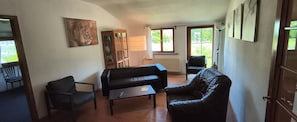 Una sala de estar con sofá, sillón y mesa de centro. Hay una estantería, una lámpara y un cuadro en la pared.