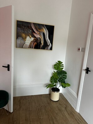 Een kamer met een houten vloer, een potplant, een deur en een abstract schilderij in een lijst aan de muur.