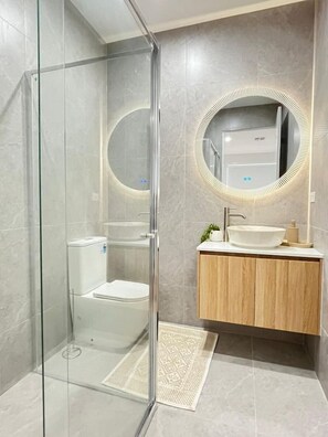 Ein modernes Badezimmer mit Glasdusche, Holzwaschtisch und rundem Spiegel mit beleuchtetem Rahmen.