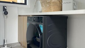 Uma área de lavanderia compacta com máquina de lavar, secadora, cesto de roupa e embalagem de detergente.