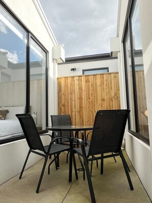 A modern outdoor patio with a glass table and chairs, a wooden fence, and a view of a building. - Modern 4BR Family Home in Wollert, VIC (Wollert)