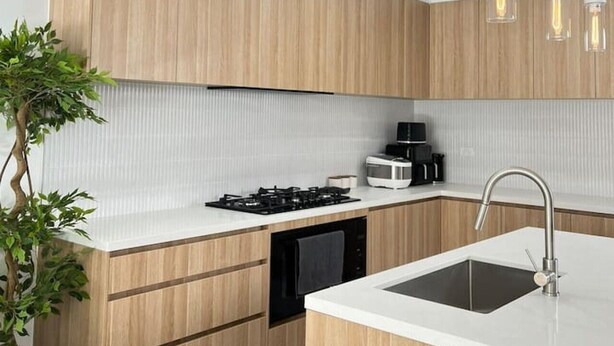 Cozinha moderna com armários de madeira, ilha central com pia, fogão e luminárias pendentes.
