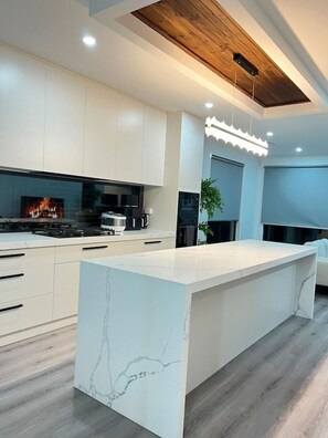 A modern kitchen with white cabinetry, a marble island, and a wooden ceiling. - Boutique 4BR Haven - Wollert Family Home (Wollert)