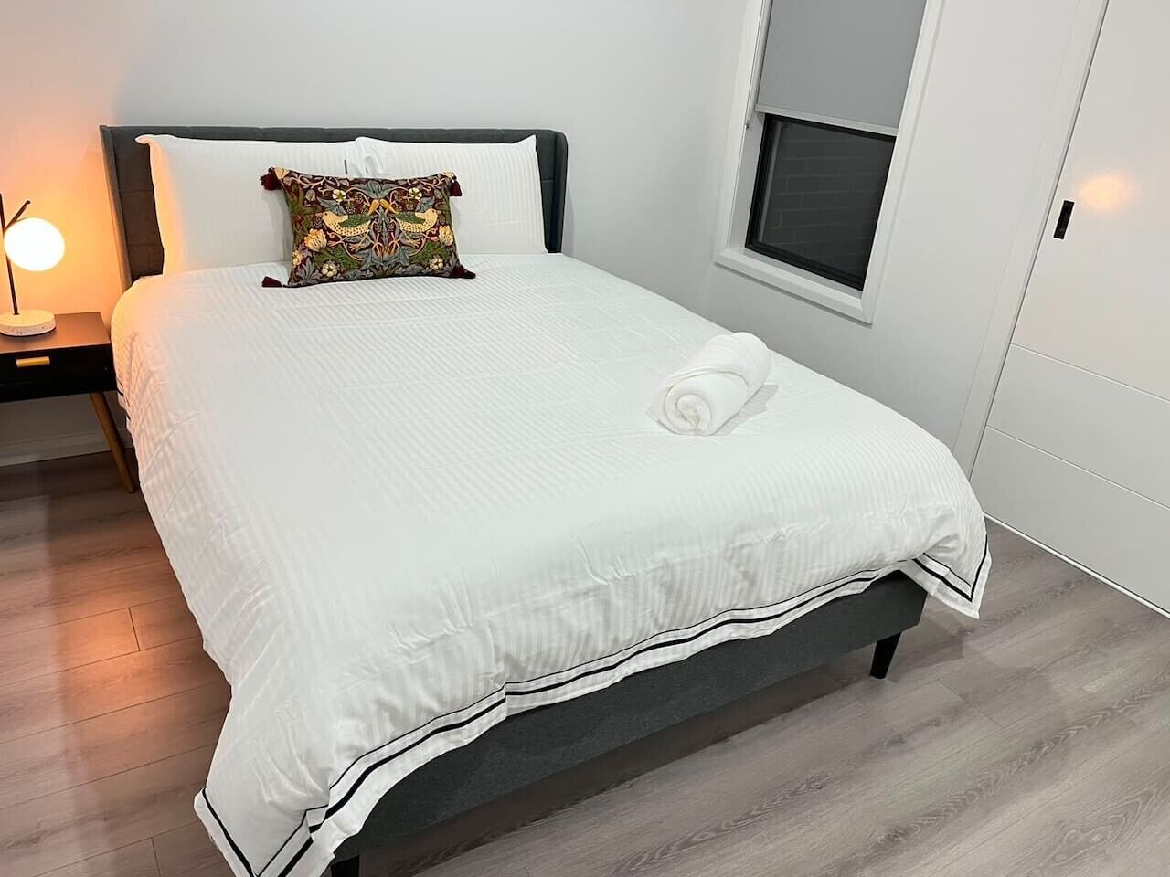 Un lit bien fait, avec une couette blanche, un coussin décoratif et une lampe de chevet.