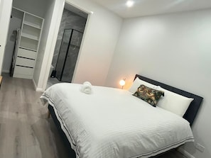 Une chambre à coucher comprenant un lit, une table de chevet, une lampe, une armoire et un espace douche.