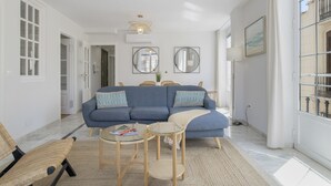 A modern living room with a blue sofa, a glass coffee table, and a dining area with a round table.