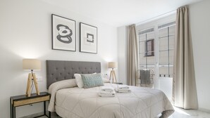 A hotel room with a large bed, two bedside lamps, a headboard, and a window with curtains.