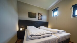 Een slaapkamer met twee bedden, een nachtkastje, een aan de muur hangend kunstwerk en een raam.