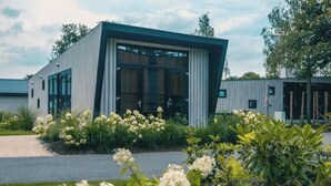 Een modern gebouw met grote ramen, een grindpad en omliggend groen.