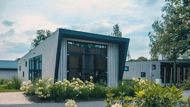Een modern gebouw met een grote glazen ingang, omgeven door keurig onderhouden tuinen en een grindpad.