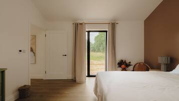 A bedroom with a bed, a chair, a lamp, a window with curtains, and a door.