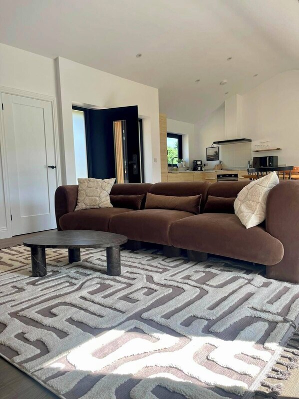 Ein modernes Wohnzimmer mit einem braunen Sofa, einem runden Couchtisch und einem gemusterten Teppich.